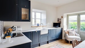 Une cuisine moderne avec des meubles de couleur sombre, un plan de travail blanc et une fenêtre qui laisse entrer la lumière naturelle.