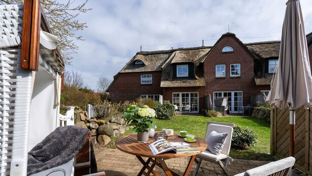 A cozy outdoor seating area with a table, chairs, and a garden view of a house with a thatched roof.