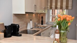 A modern kitchen with wooden cabinets, a stainless steel sink, a coffee machine, a wine bottle, and a vase with flowers.