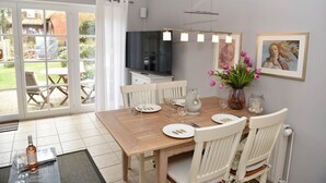 A dining area with a wooden table, white chairs, a TV, and a view of the outdoors.