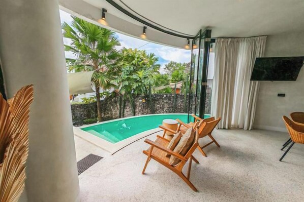 A room with a pool, two wicker chairs, a TV, and a view of palm trees. - Hillstone Luxury Village (Bali)