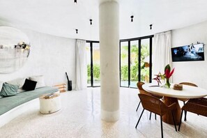 A modern living room with a sofa, a dining table with chairs, a large pillar, and a TV on the wall. - Hillstone Luxury Village (Bali)
