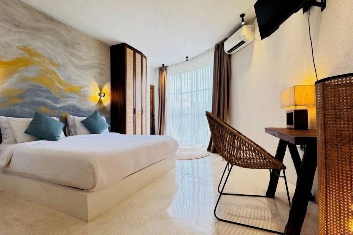 Une chambre d’hôtel équipée d’un lit, d’un bureau, d’une chaise, d’une grande fenêtre et d’un climatiseur fixé au mur.
