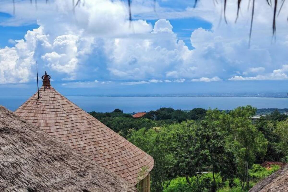 Un bâtiment à toit de chaume, avec vue sur une étendue d’eau et une végétation luxuriante en arrière-plan.