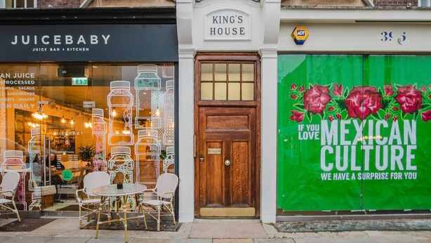 A storefront with 'JUICEBABY' and 'KING'S HOUSE' signs, a wooden door, and a green advertisement for Mexican culture.