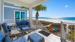 A covered outdoor seating area with blue patterned cushions, a wooden bench, and a view of the beach and ocean. - Sea Glass - Huge Ocean Front Home with Gulf Views, Private Pool & Direct Beach Access (Miramar Beach)