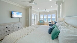 A bedroom with a large bed, a TV mounted on the wall, and a view of the ocean through the windows. - Sea Glass - Huge Ocean Front Home with Gulf Views, Private Pool & Direct Beach Access (Miramar Beach)