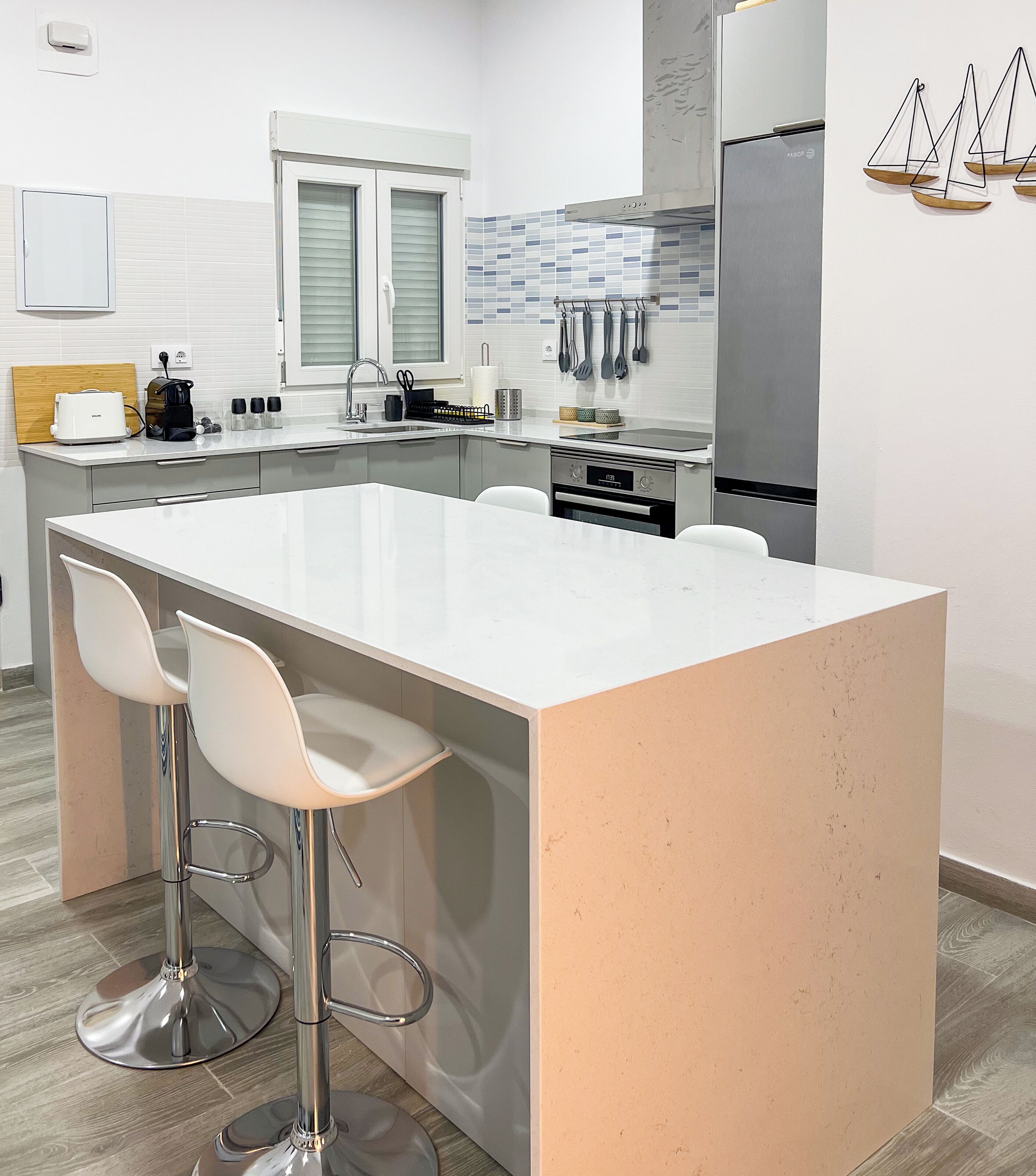 Une cuisine moderne dotée d’un grand îlot central, de deux tabourets de bar, d’appareils électroménagers en acier inoxydable et d’un pare-feu en carreaux.