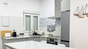 A modern kitchen with a large island, two bar stools, stainless steel appliances, and a tiled backsplash.