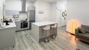 A modern kitchen with a central island, bar stools, a refrigerator, oven, and a dining table.