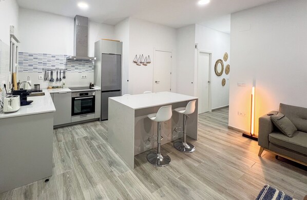A modern kitchen with a central island, bar stools, a refrigerator, oven, and a dining table.