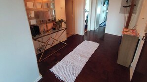 Un passadís amb sòl de fusta fosca, una catifa blanca, un penjallum i una paret amb quadres emmarcats.