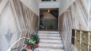 Gradi de marbre amb plantes en testos, un mural al sostre i una bústia penjada a la paret.
