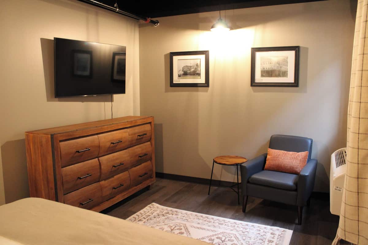 A bedroom with a wooden dresser, a single bed, a chair, and two framed pictures on the wall.