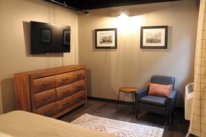 A bedroom with a wooden dresser, a single bed, a chair, and two framed pictures on the wall. - 4th Street Lofts (Bemidji)