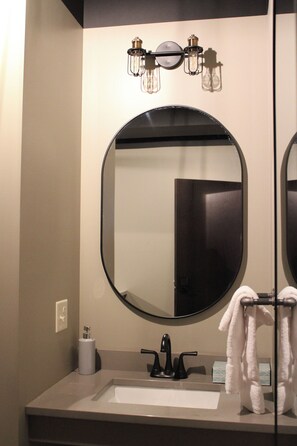 A bathroom with a round mirror, a sink, and a towel rack. - 4th Street Lofts (Bemidji)