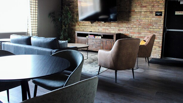 A modern living room with a brick wall, a flat-screen TV, a sofa, a coffee table, and a dining table. - 4th Street Lofts (Bemidji)