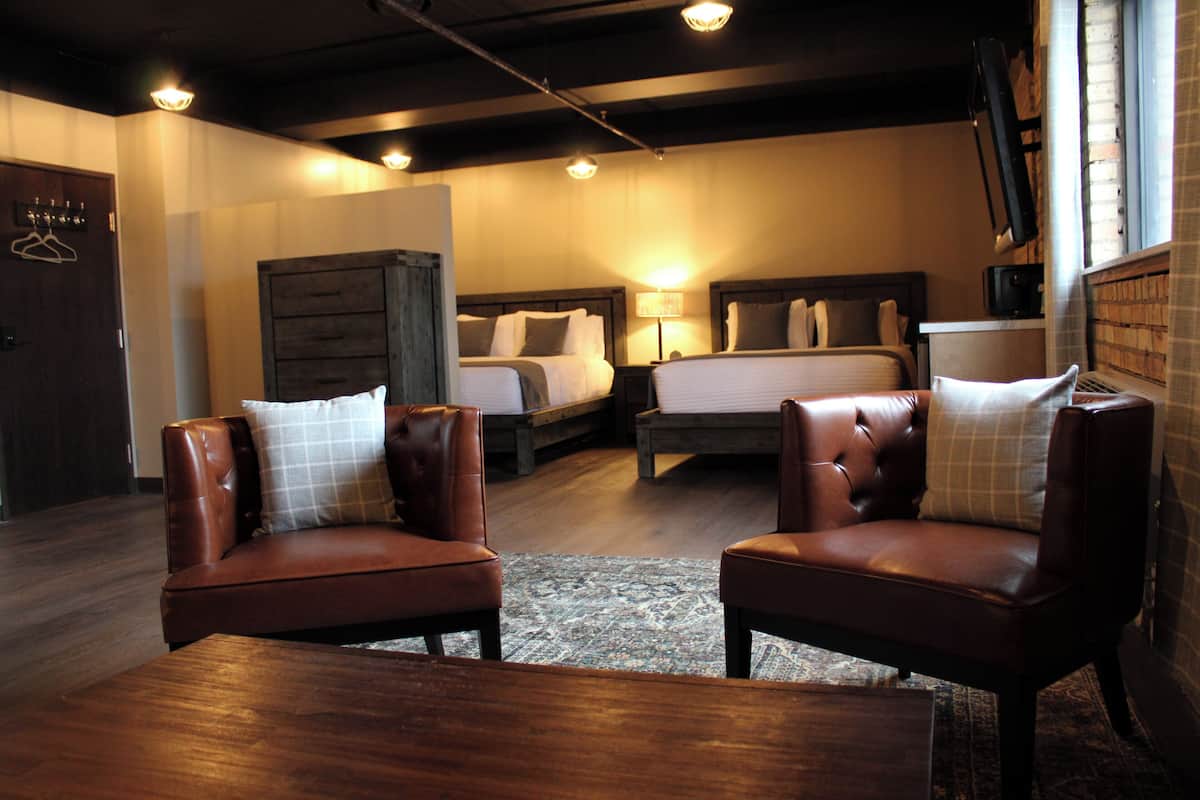 A hotel room with two leather armchairs, a wooden coffee table, a large bed with a headboard, a dresser, and a television on a stand.