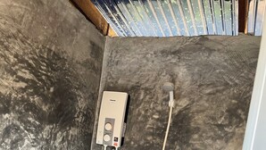 Ein Badezimmer mit grauen Fliesen, einer weißen Duschkabine und einem sichtbaren Abfluss.