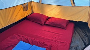 Ein Zelt mit Bett, roter Bettwäsche und zwei blauen Handtüchern.