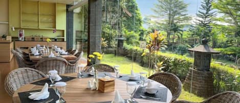 A dining area with a round table set for four, surrounded by wicker chairs, with a view of a lush garden and a traditional lantern structure.