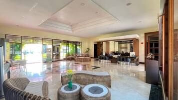 A spacious lobby with a high ceiling, a seating area with wicker furniture, and a view of the outdoors through large windows.