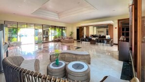 A spacious lobby with a high ceiling, a seating area with wicker furniture, and a view of the outdoors. - Grage Resort Sangkan (Cigandamekar)