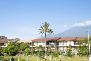A hotel with multiple buildings, a palm tree, and a mountain in the background. - Grage Resort Sangkan (Cigandamekar)