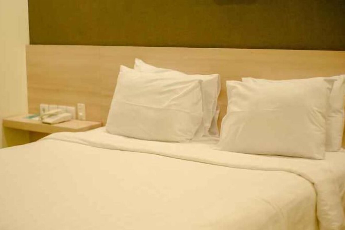 Une chambre d’hôtel avec un lit, des oreillers, une table de chevet et un téléphone.