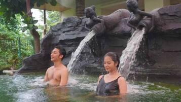 Two people in a water feature with a rocky backdrop and statues.