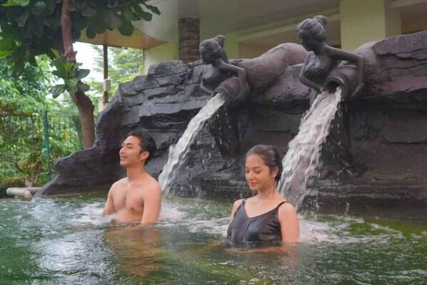 Two people in a water feature with a rocky backdrop and statues. - Grage Resort Sangkan (Cigandamekar)
