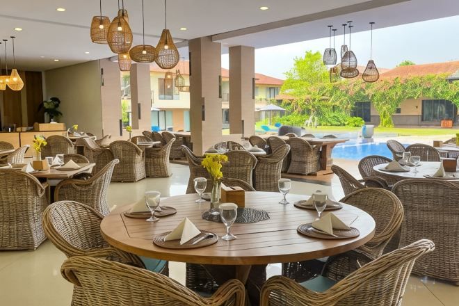 Un restaurant avec des tables rondes et des chaises en osier, une piscine en arrière-plan et des lampes suspendues.