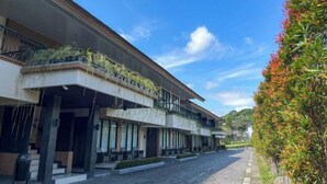 A modern hotel with a covered outdoor seating area, a stone-paved courtyard, and a clear blue sky. - Grage Resort Sangkan (Cigandamekar)