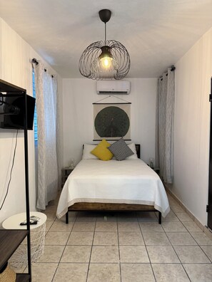 Ein Schlafzimmer mit einem Bett, einer Wand-Klimaanlage, einer dekorativen Leuchte und gemusterten Vorhängen.
