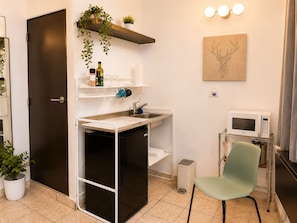 Una cocina compacta con refrigerador, lavamanos, microondas y una silla.