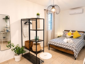 Un dormitorio con una cama, una estantería, una lámpara colgante y una ventana con cortinas.
