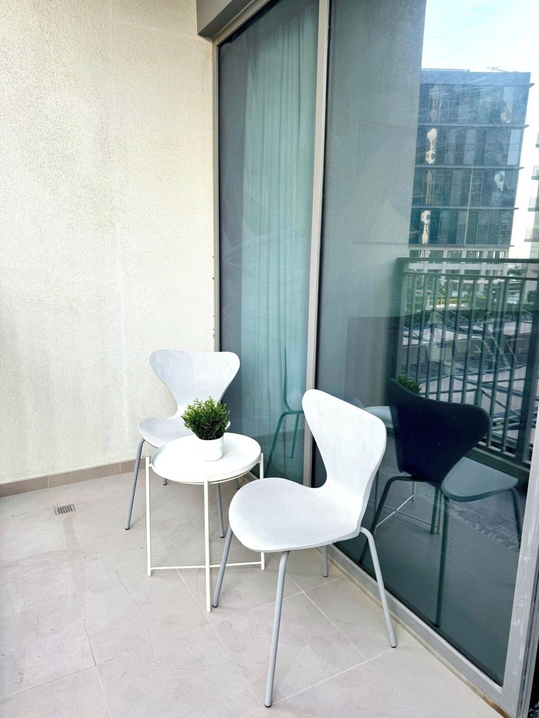 A balcony with two white chairs and a small table with a plant.
