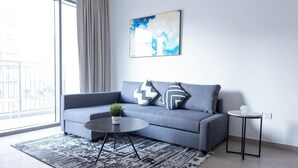 Een moderne woonkamer met een grijze bank, een ronde salontafel, een klein bijzettafeltje en een schilderij aan de muur.