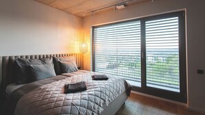 Ein Schlafzimmer mit einem großen Bett, einem Kopfteil, einem Fenster mit Jalousien und einer Wandleuchte.