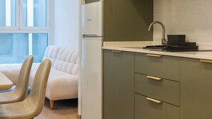 A compact kitchen with a built-in refrigerator, a sink with a faucet, and a dining area with a sofa and chairs.