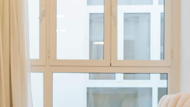 A corner sofa with a light-colored, tufted design, positioned in front of a large window with a view of a building.
