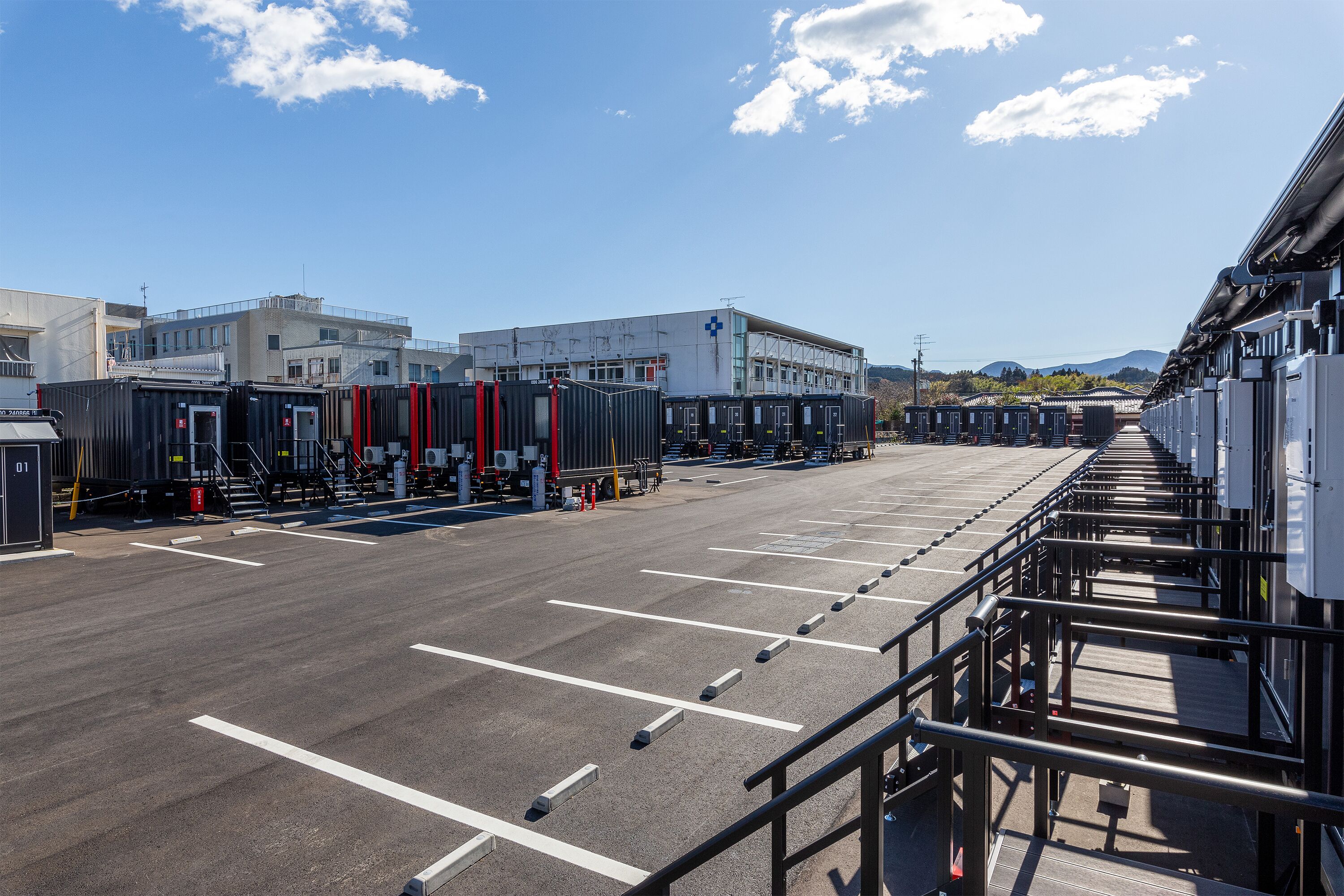 Uma área de estacionamento com fileiras de vagas e um edifício com fachada branca e emblema de cruz azul.