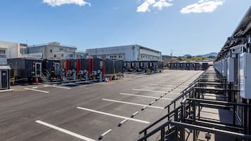 Uma área de estacionamento com fileiras de vagas e um edifício com fachada branca e emblema de cruz azul.