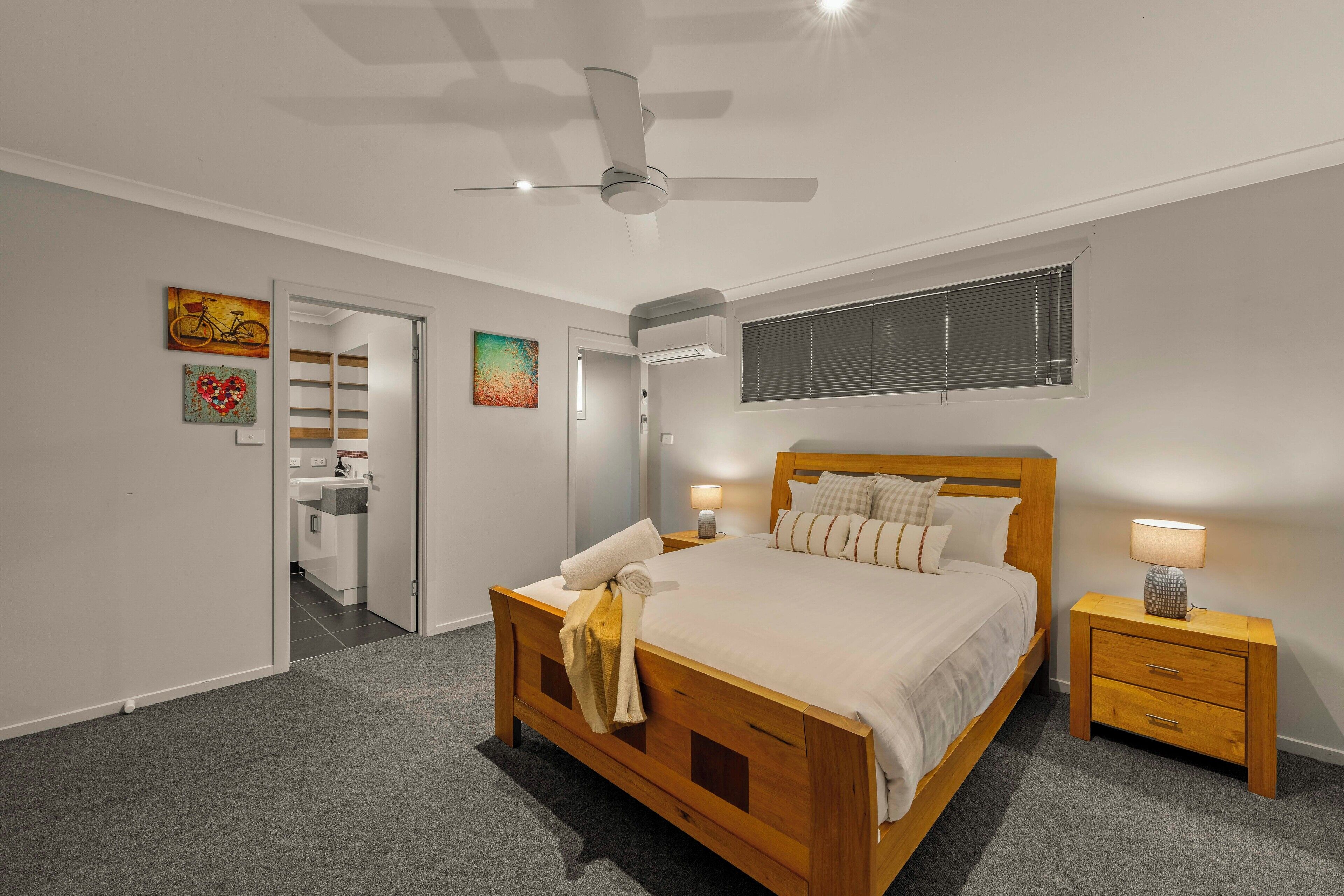 Un dormitorio con cama de madera, mesitas de noche, ventilador de techo y obras de arte en las paredes.