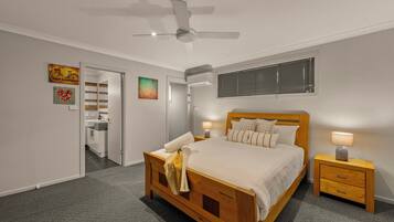 Un dormitorio con cama de madera, mesitas de noche, ventilador de techo y obras de arte en las paredes.