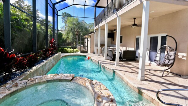 A swimming pool with a stone edge, a covered patio area with outdoor furniture, and a glass-enclosed structure. - Azure Sky Spacious 5-bedroom house with WiFi and AC in enchanting Naples (Naples)