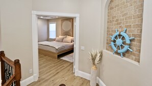 A bedroom with a wooden floor, a bed, a wall-mounted ship's wheel, and a vase with dried plants. - Azure Sky Spacious 5-bedroom house with WiFi and AC in enchanting Naples (Naples)