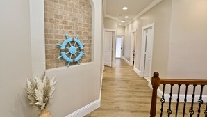A hallway with a brick accent wall, a blue ship's wheel decoration, and a wooden railing. - Azure Sky Spacious 5-bedroom house with WiFi and AC in enchanting Naples (Naples)