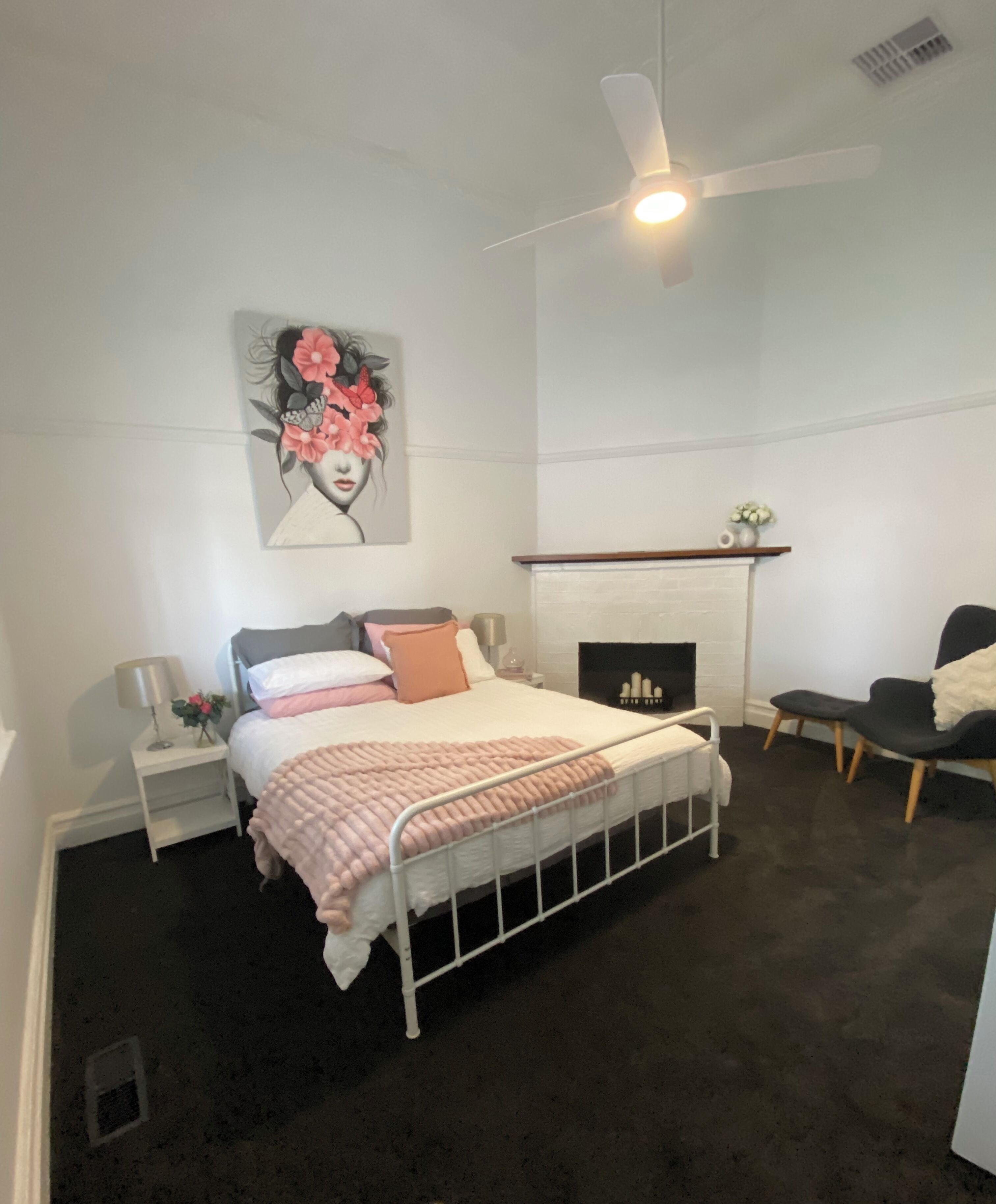 Une chambre à coucher comprenant un lit, des tables de chevet, une commode, une chaise, une cheminée et un ventilateur de plafond.