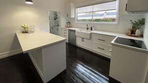 A modern kitchen with white cabinets, a large window, and a dark wooden floor. - Daisy Cottage - 4 bedrooms, Close to CBD (Golden Square)